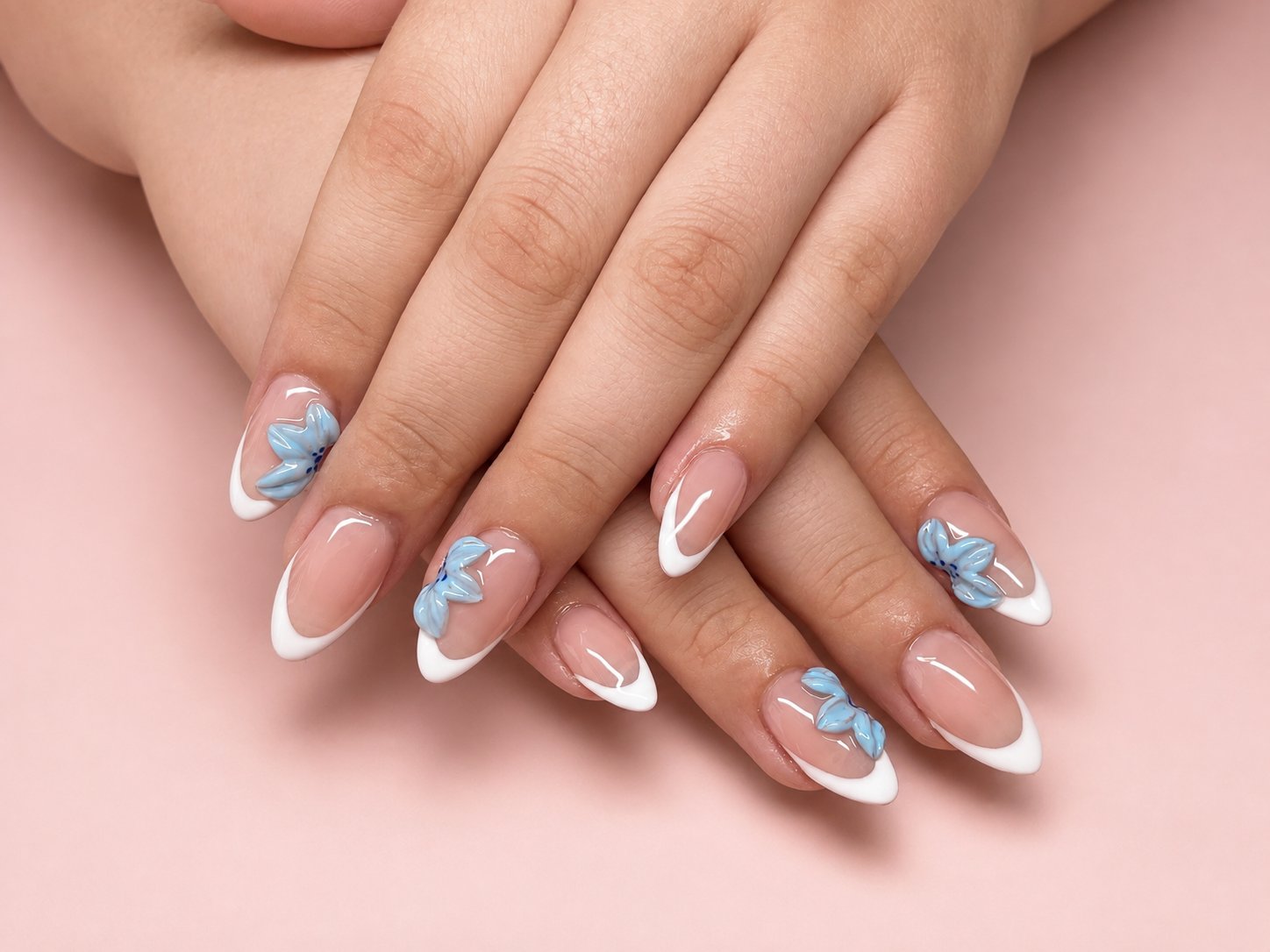 Almond nails with crisp white french tips and sculpted three-dimensional blue flowers
