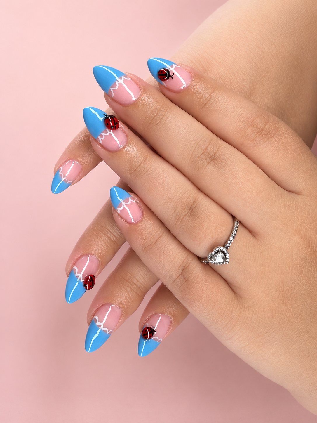 Almond nails with sky-blue french tips, fine white lace lines, and tiny painted ladybirds