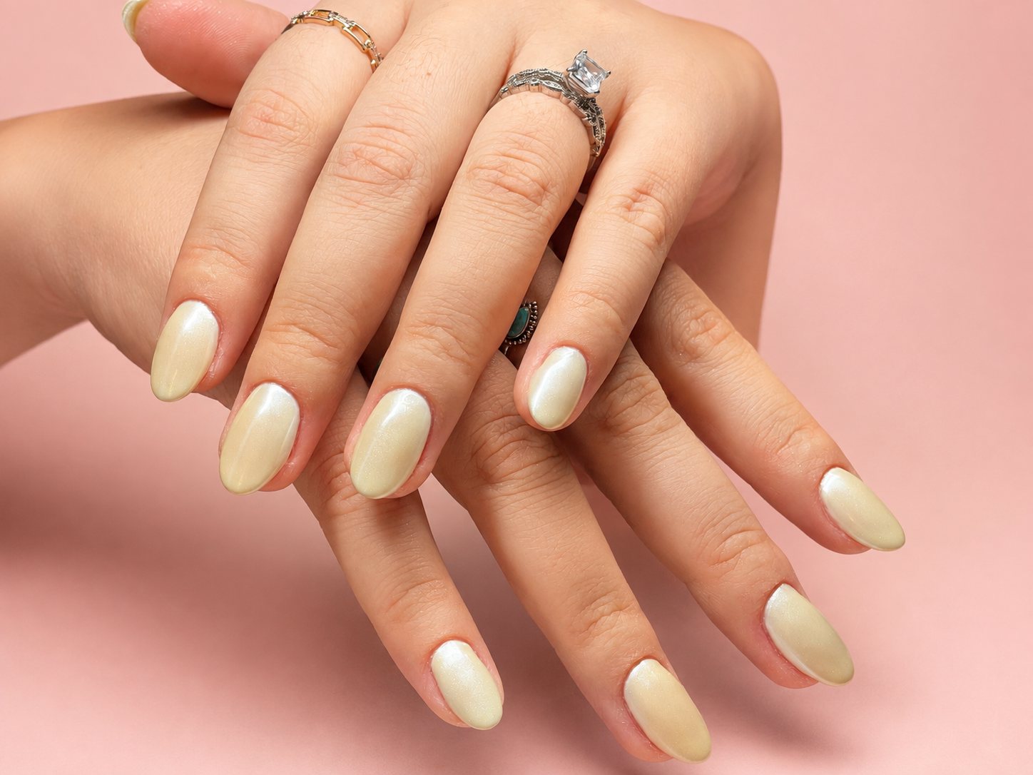 Crossed hands wearing a soft pearl-cream manicure and delicate rings
