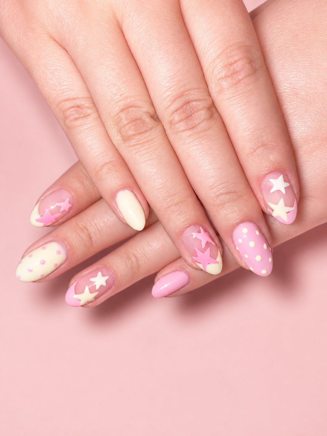 Almond nails in pastel pink and cream with painted stars and polka dots