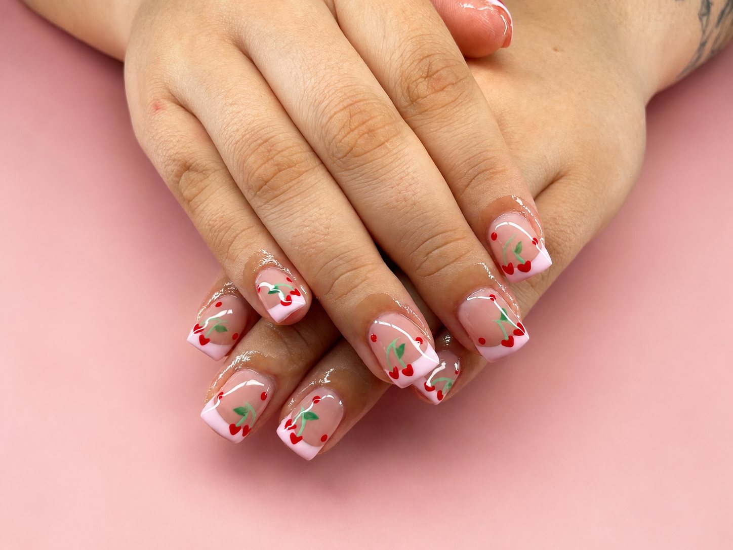 Short square nails with soft pink french tips and hand-painted cherries and hearts