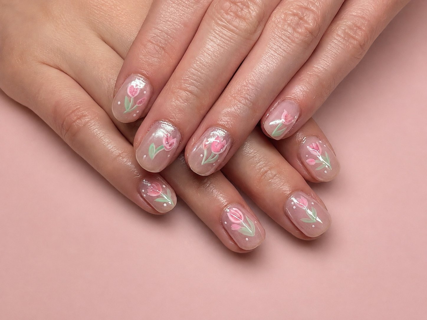 Short GelX manicure with hand-painted pink tulips and pale green stems on a sheer base
