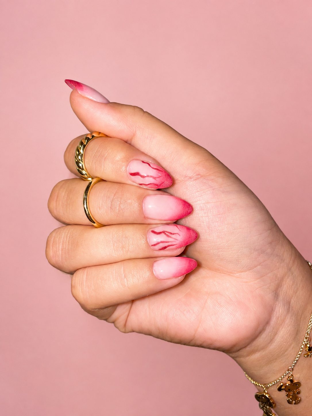 Long almond nails in pink ombre with hand-painted hearts, flowers, and glitter fades