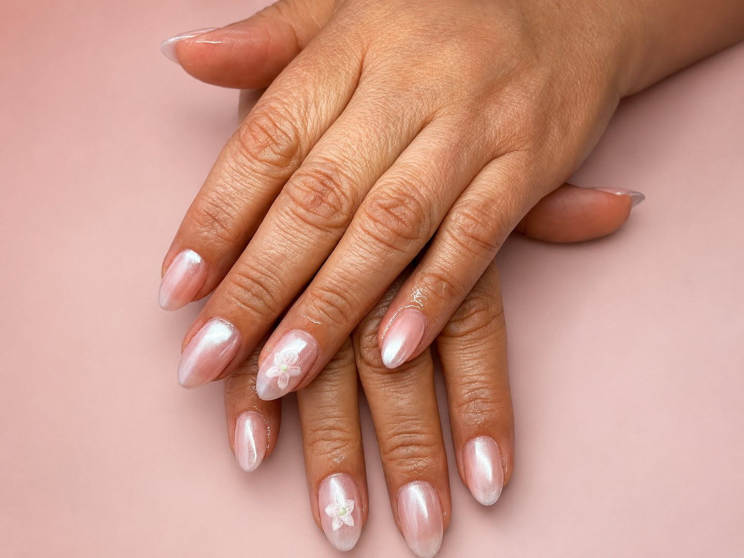 Almond nails in pearlescent white, each hand carrying a single painted flower accent